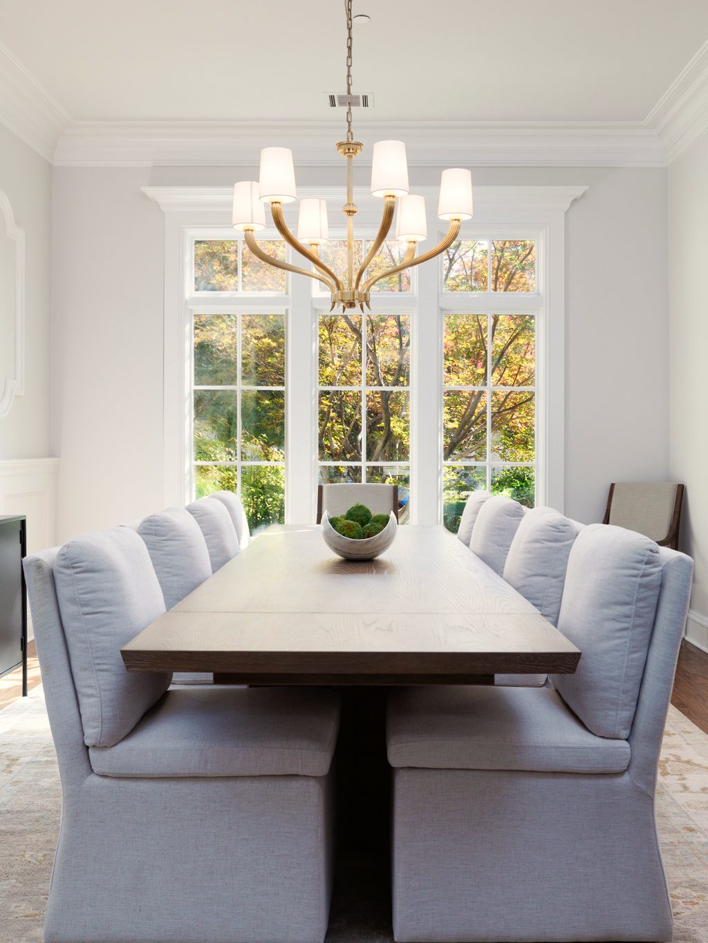 A light-filled dining room with a long table and a brass chandelier, designed by Anna